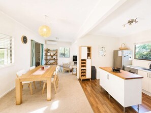 A modern kitchen with white cabinetry, a wooden dining table, and a built-in wine rack. - Blue Chill of Mollymook (Mollymook Beach)