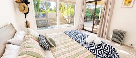 A bedroom with a bed, pillows, a hat on the wall, and a view of the outdoors through large windows.