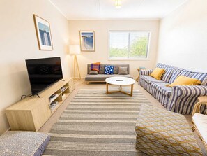 A living room with a television, sofa, and striped couch. - Blue Chill of Mollymook (Mollymook Beach)