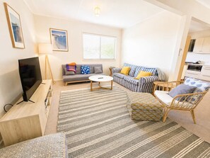 A modern living room with a flat-screen TV, sofas, a coffee table, and a wicker chair. - Blue Chill of Mollymook (Mollymook Beach)