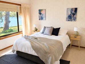 Un dormitorio con una cama, dos mesitas de noche, un ventanal con cortinas y dos cuadros abstractos en la pared.