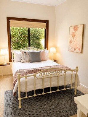 Een slaapkamer met een bed, twee bedlampen, een raam met uitzicht op groen en een kunstwerk in een lijst aan de muur.