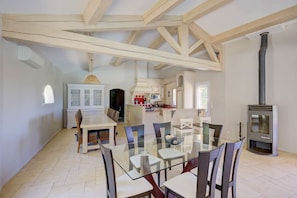 A dining area with a glass table and chairs, a kitchen with white cabinets, and a wood-burning stove. - Une Parenthèse d’Exception au Cœur du Var Authentique (FLAYOSC)