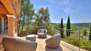 Ein Balkon mit Korbmöbeln, einem Geländer und Blick auf eine bewaldete Landschaft.
