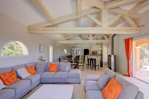 A modern living room with a sectional sofa, a dining area, and a kitchen in the background. - Une Parenthèse d’Exception au Cœur du Var Authentique (FLAYOSC)
