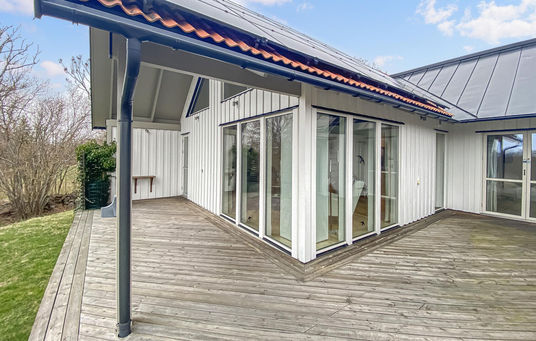 Ett modernt hus med en täckt uteplats, stora skjutbara glasdörrar och ett trädäck.