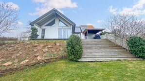 A modern house with a large front porch, a wooden staircase, and a well-maintained lawn.