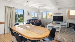 A spacious living room with a wooden dining table, black chairs, a black sofa, a television, and a fireplace. - MeNo's at Bawley Point (Bawley Point)