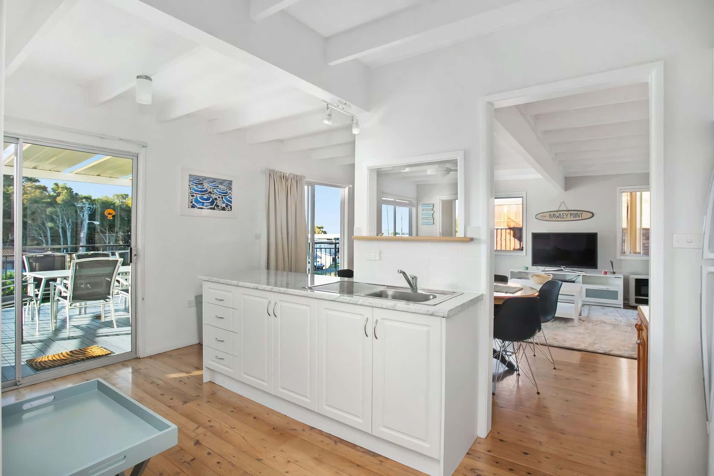 A modern kitchen with white cabinetry, a built-in sink, and a dining area with a table and chairs.