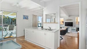 A modern kitchen with white cabinetry, a built-in sink, and a dining area with a table and chairs. - MeNo's at Bawley Point (Bawley Point)