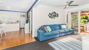 A modern living room with a blue sofa, a coffee table, and a dining area with a table and chairs. - Mollymook Beach Cottage (Mollymook Beach)