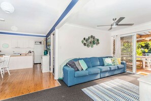 Ein modernes Wohnzimmer mit blauem Sofa, Essbereich und Küche mit weißen Schränken.