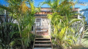 A house with a wooden staircase leading to a door with a metal gate. - Mollymook Beach Cottage (Mollymook Beach)