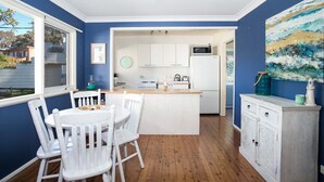 A kitchen with white cabinets, a central island with seating, a microwave, and a refrigerator. - Mollymook Beach Cottage (Mollymook Beach)