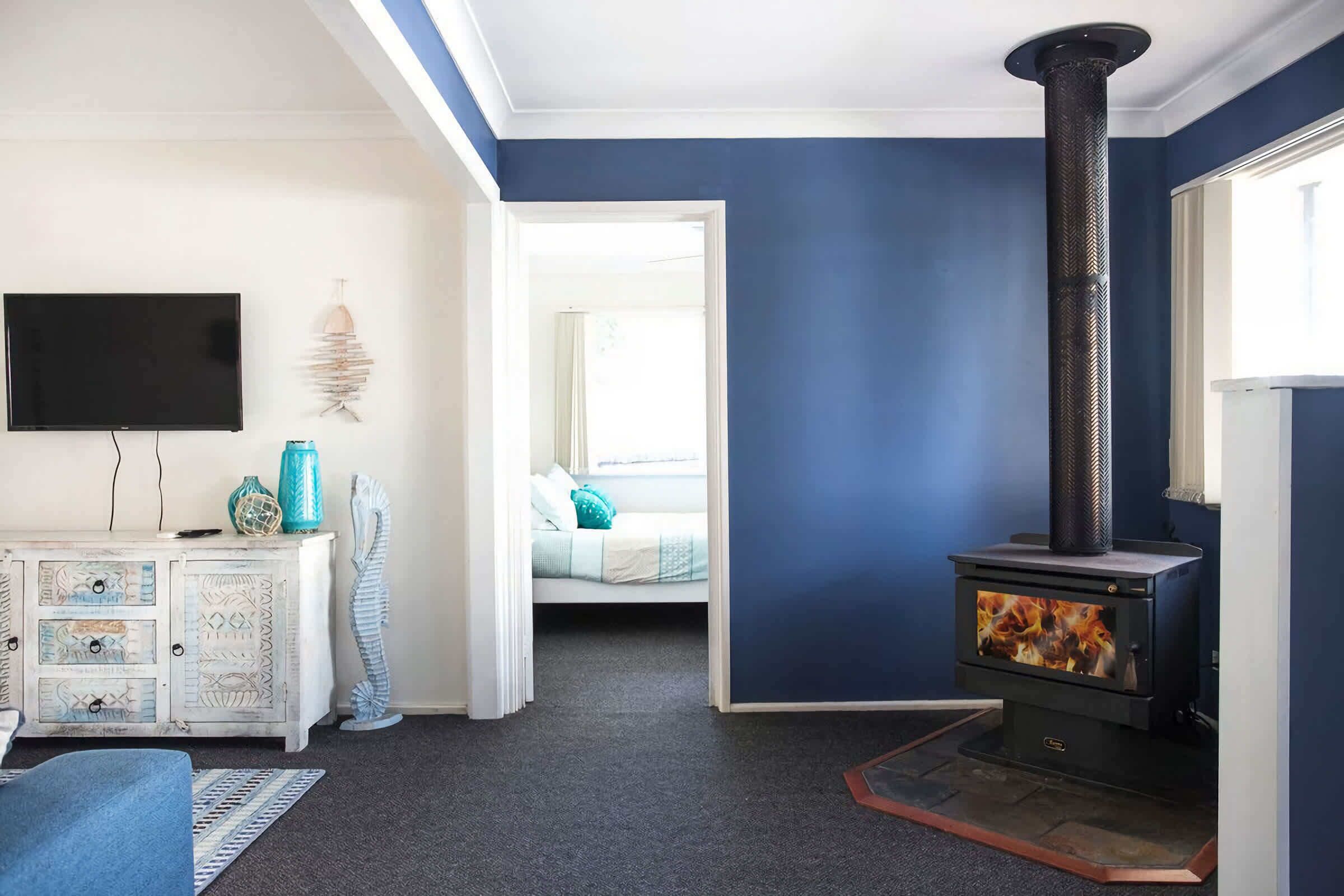 A living room with a fireplace, a television, and a bed in the background.