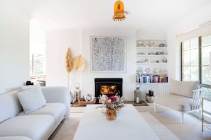 Ein Wohnzimmer mit weißem Sofa, einem weißen Couchtisch, einem Kamin und einem Bücherregal.