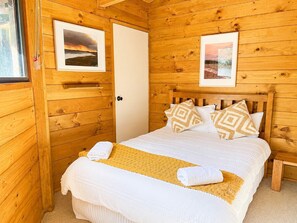 Ein Zimmer mit Holzboden, einem Bett, zwei gerahmten Bildern und einer Tür.