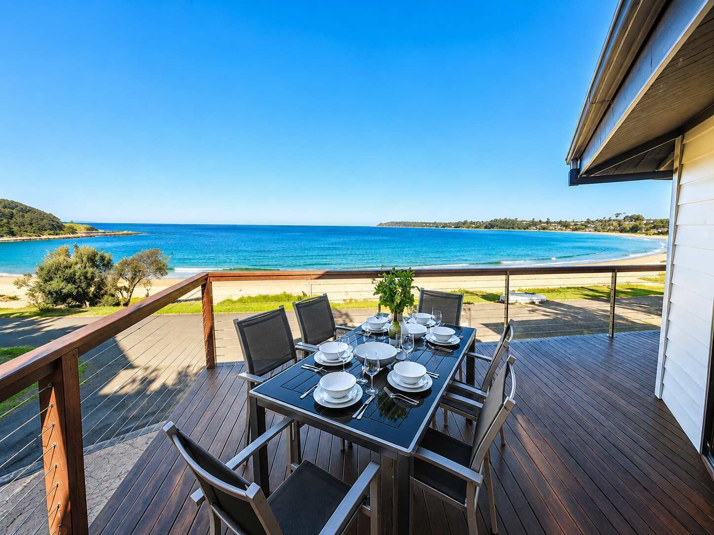 A dining table set on a wooden deck with a view of the ocean.