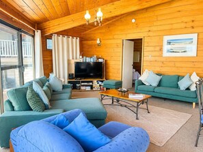 A cozy cabin interior with a large sectional sofa, a television, and a wooden ceiling. - Ocean's Kiss at Mollymook (Mollymook Beach)
