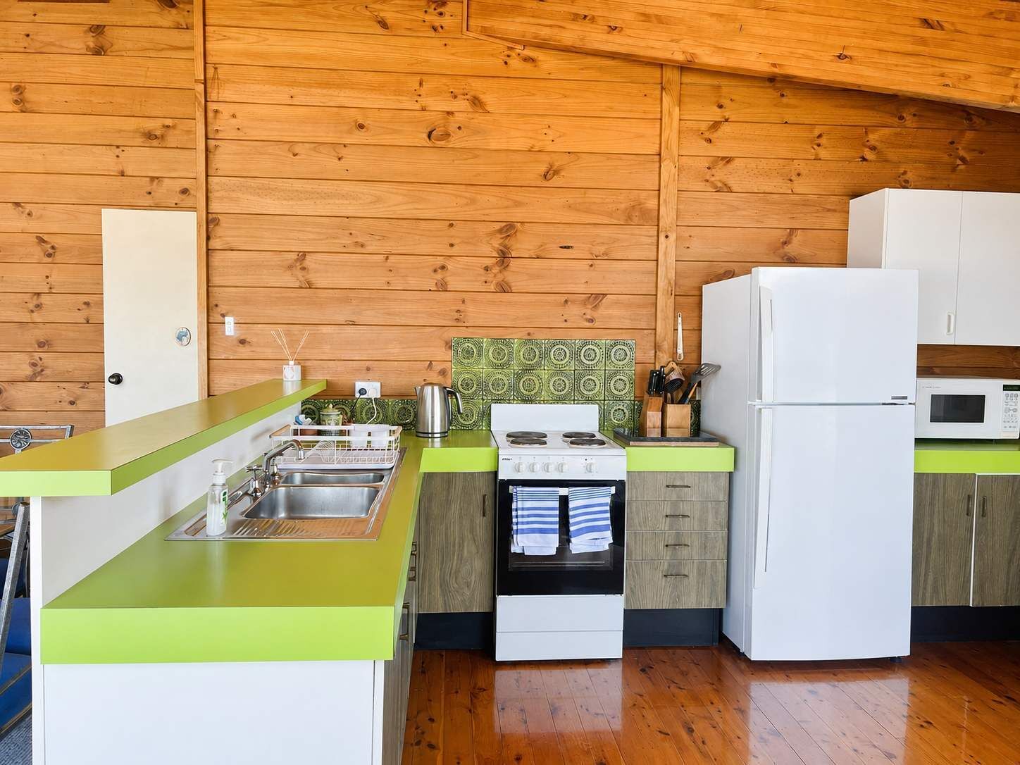 Une cuisine compacte avec des murs en bois, un plan de travail vert, une cuisinière, un évier et un réfrigérateur.