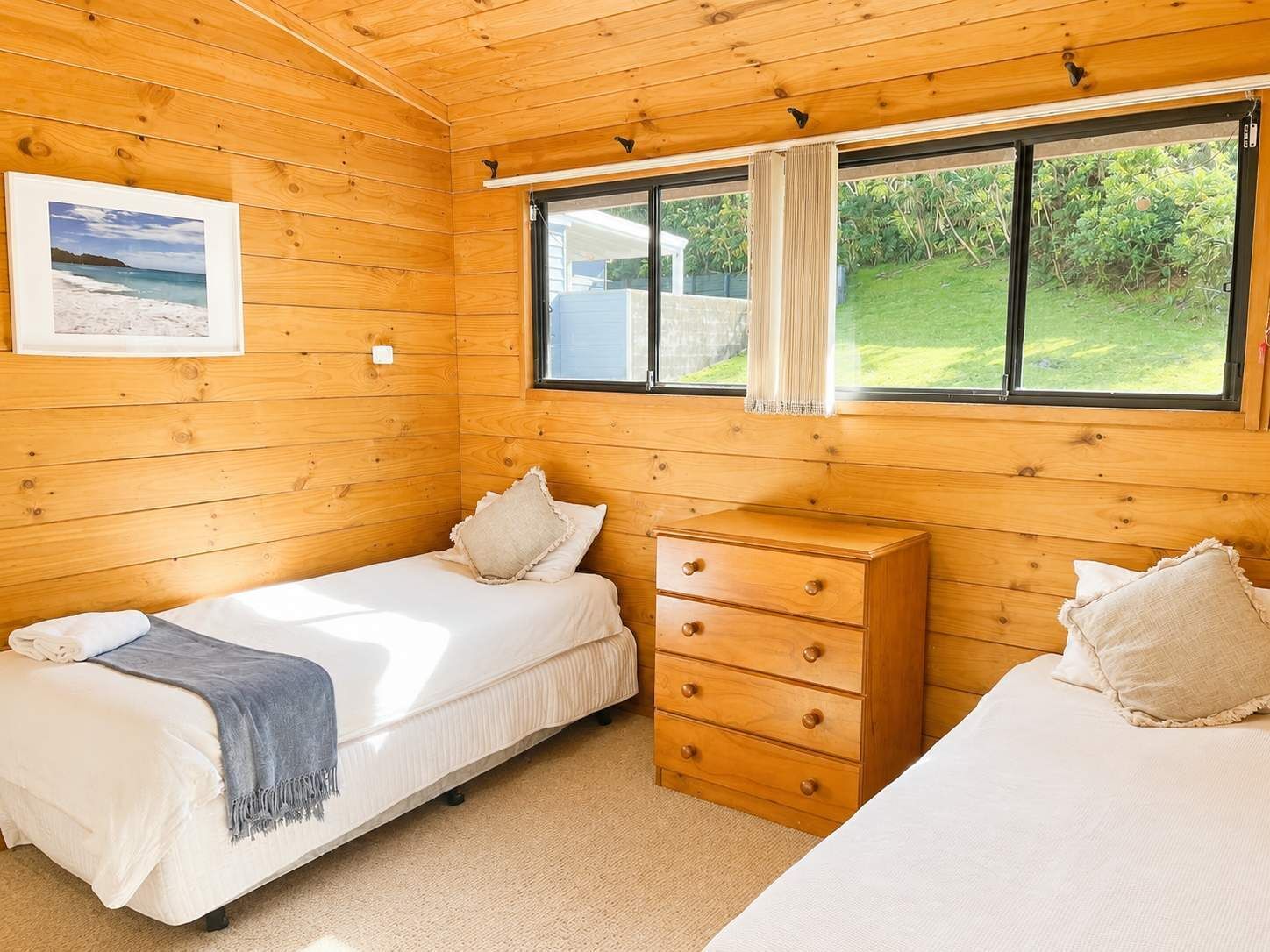 Ein blockhaushaltsähnliches Zimmer mit zwei Betten, einer Holzkommode und einem Fenster mit Blick auf Grünflächen.