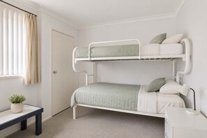 A bunk bed with a desk and a plant in a room with white walls and a door.