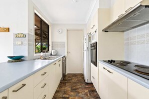 A kitchen with a stove, oven, and sink. There is a window with a view of greenery outside. - Reflections at Lake Conjola (Lake Conjola)