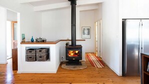 A modern kitchen with a wood-burning stove, a stainless steel refrigerator, and a wooden floor. - Sea Forever at Kioloa (Kioloa)