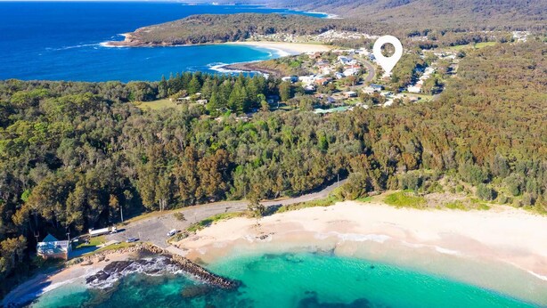 An aerial view of a coastal area with a beach, forested hills, and a small settlement. - Sea Forever at Kioloa (Kioloa)