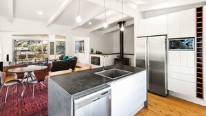 A modern kitchen with a central island, stainless steel appliances, and a dining area with a red patterned rug. - Sea Forever at Kioloa (Kioloa)