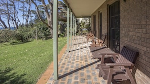 A covered outdoor seating area with brick flooring and wooden benches, adjacent to a brick building with large windows. - Ocean's Edge at Bawley Beach (Bawley Point)