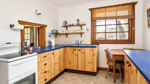 A kitchen with wooden cabinets, a blue countertop, a sink, and a window with a view of trees.