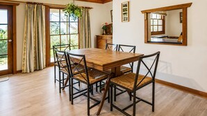 Uma sala de jantar com mesa e cadeiras de madeira, janelas amplas com cortinas e um espelho na parede.