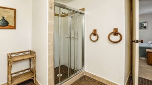 A bathroom with a glass-enclosed shower, a wicker shelf, and two wooden towel rings on the wall.