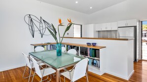 A modern kitchen with white cabinets, a wooden countertop, and a glass dining table with chairs. - Ohana Kioloa at Kioloa Beach (Kioloa)