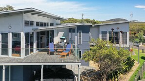 A modern two-story house with a covered patio, large windows, and a view of a hilly landscape. - Ohana Kioloa at Kioloa Beach (Kioloa)