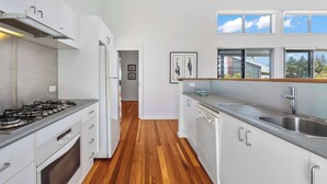 A modern kitchen with white cabinets, a stainless steel sink, and a window overlooking the outdoors. - Ohana Kioloa at Kioloa Beach (Kioloa)