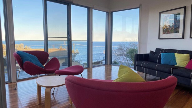A modern living room with large windows, a wooden floor, and a view of the sea. - Ohana Kioloa at Kioloa Beach (Kioloa)