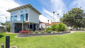A modern two-story house with a balcony, a well-maintained lawn, and a variety of plants. - Ohana Kioloa at Kioloa Beach (Kioloa)