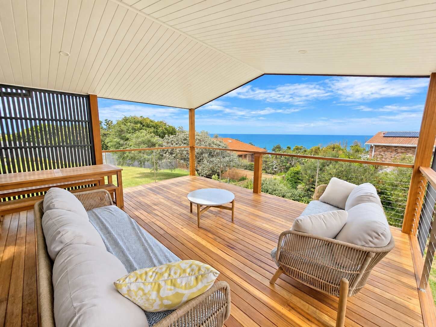 Une terrasse extérieure avec un plancher en bois, des meubles en osier et une vue sur l’océan.