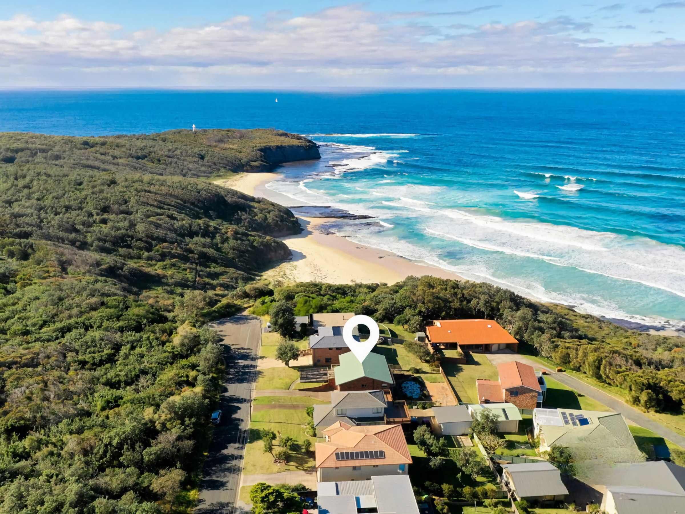 Vista aérea de una zona residencial costera con casas, un faro y una playa.