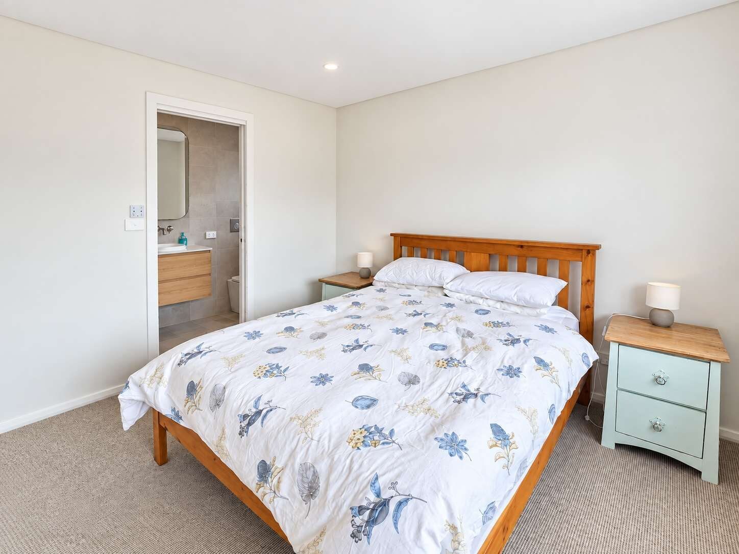 A bedroom with a bed, nightstands, a wooden headboard, a bathroom with a mirror, and a door.