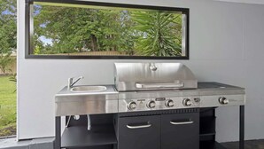 A kitchen with a built-in sink, a stainless steel grill, and a window overlooking a garden.