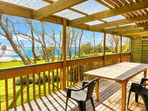 Une terrasse en bois avec une table et des chaises, donnant sur une plage et une forêt.