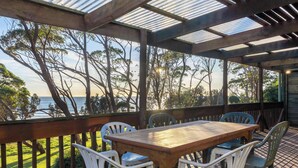 Un espacio exterior techado con una mesa y sillas de madera, con vistas a un cuerpo de agua y árboles.
