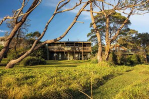 A building with a balcony, surrounded by trees and grass. - Ocean Beach House at Bawley Point (Bawley Point)