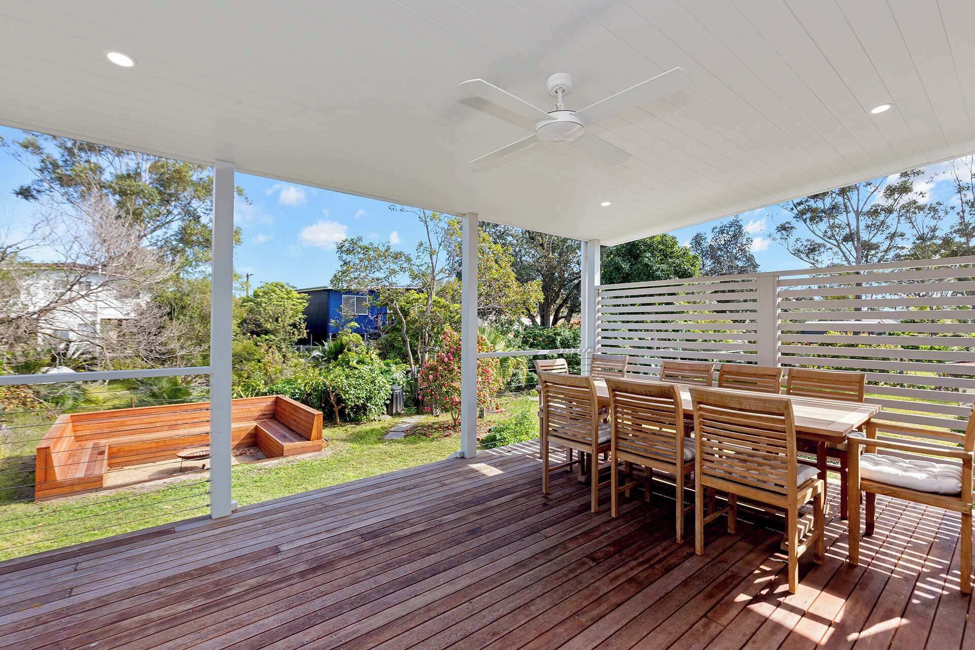 A covered outdoor area with a wooden deck, a table with chairs, and a white ceiling fan.