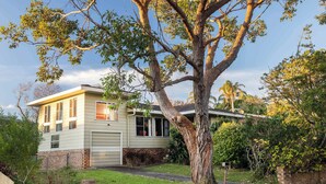A two-story house with a brick foundation, a large tree in front, and a well-maintained lawn. - Seaview Escape at Gannet (Bawley Point)