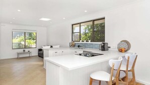 Una cocina moderna con armarios blancos, una isla grande con taburetes de bar, un ventanal con vista a zonas verdes y una estufa empotrada.