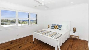 Un dormitorio con una cama blanca, un ventilador de techo y una ventana con persianas.